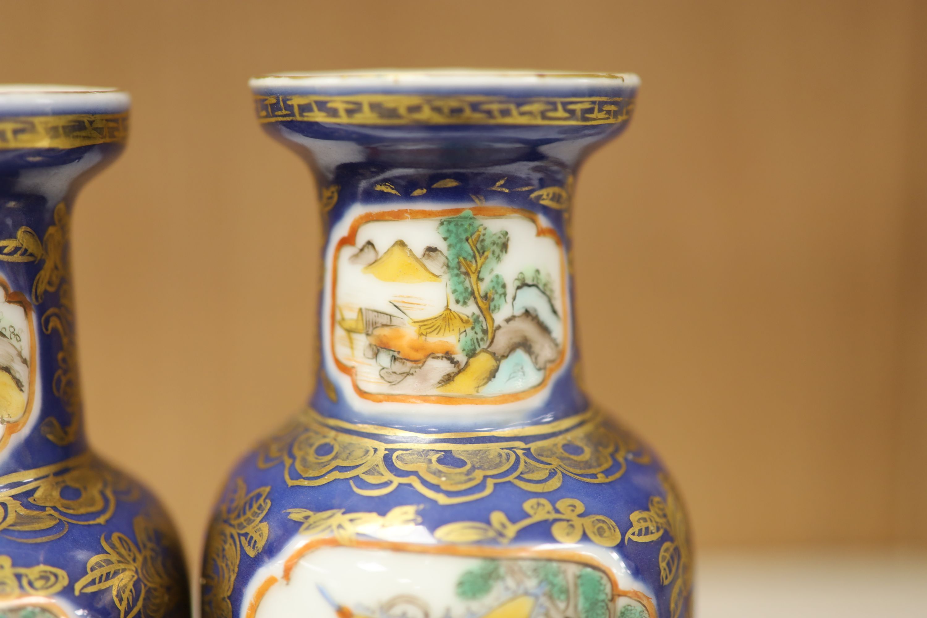 A pair of Chinese Kangxi style blue-ground vases, late 19th century decorated with panels of warriors and heightened in gilt, on carved hardwood stands, height 18cm excluding stand